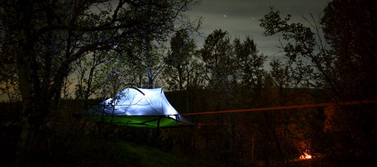 Foto: Hans Ola Østby. Å^sove i et telt slått opp mellom trærne mens du ser på stjernene .